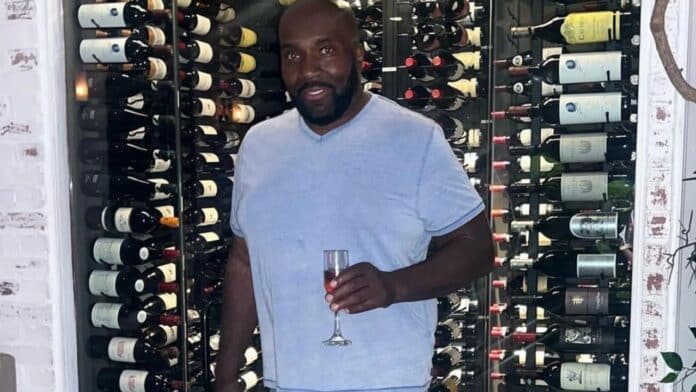 Man poses near wine bottle shelf