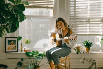 Woman strums guitar by sunlit window